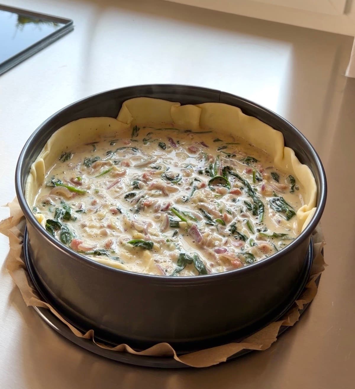 Zwiebel-Spinat-Quiche mit Speck vor dem Backen in einer Springform