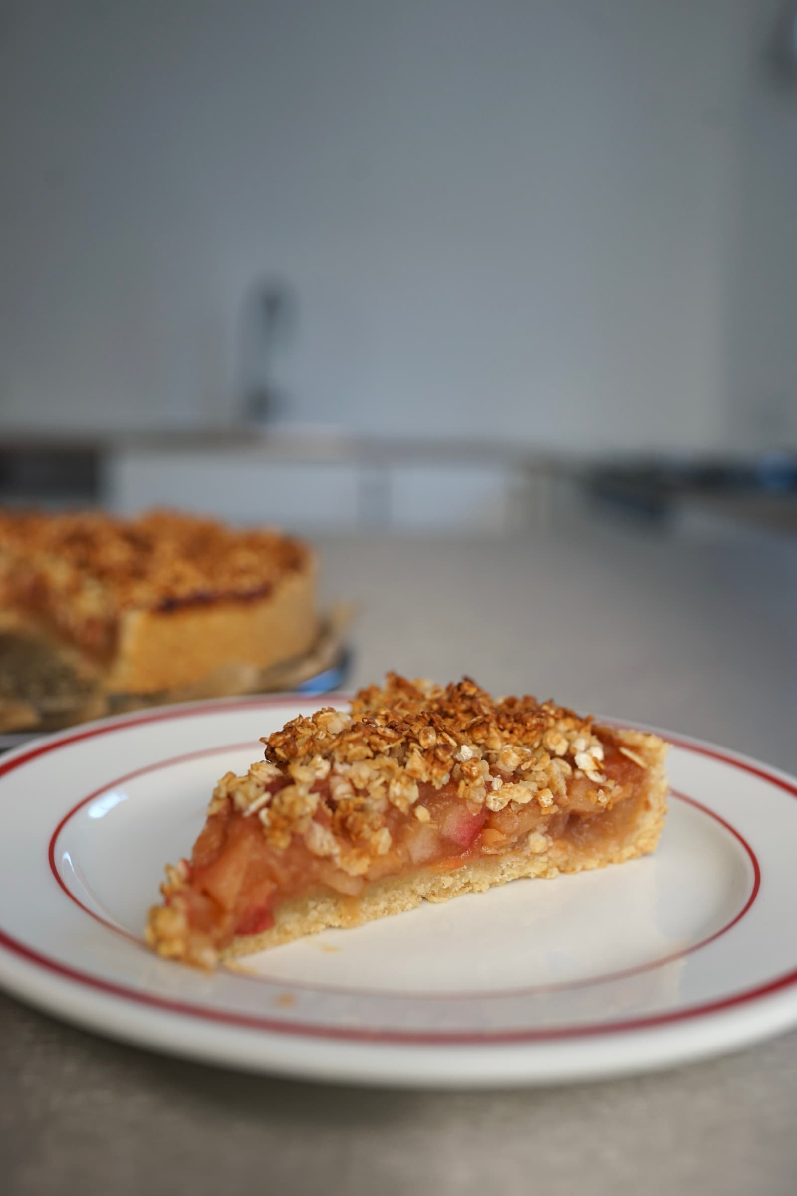 Stück Apfelkuchen mit Haferstreuseln, der ganze Kuchen im Hintergrund